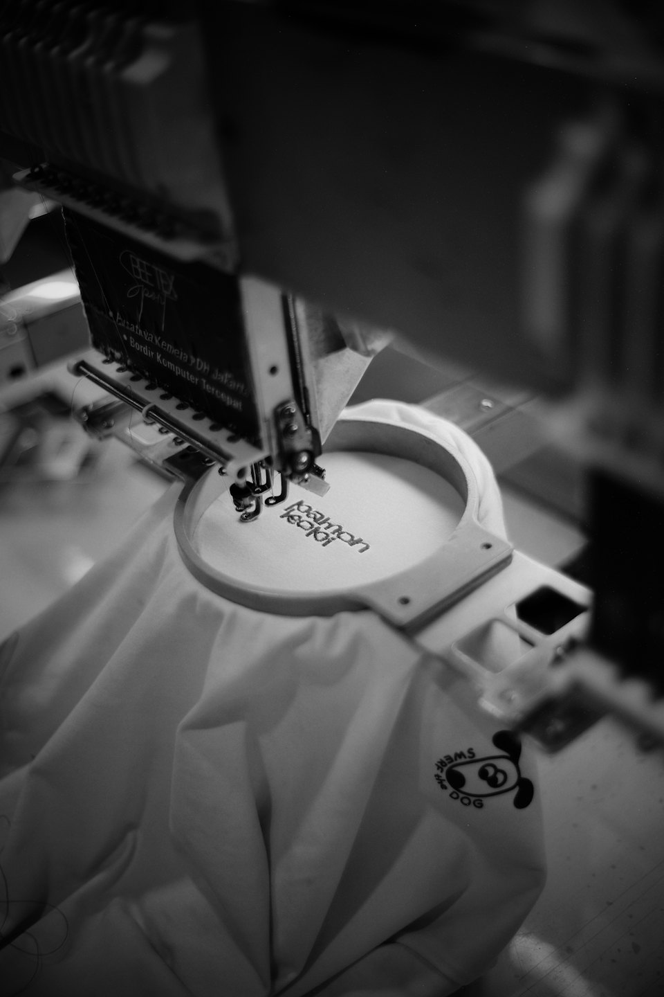 Una macchina da ricamo industriale cuce testo su tessuto teso.