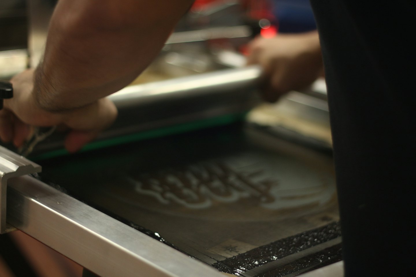 Mani che azionano un torchietto serigrafico con inchiostro scuro.