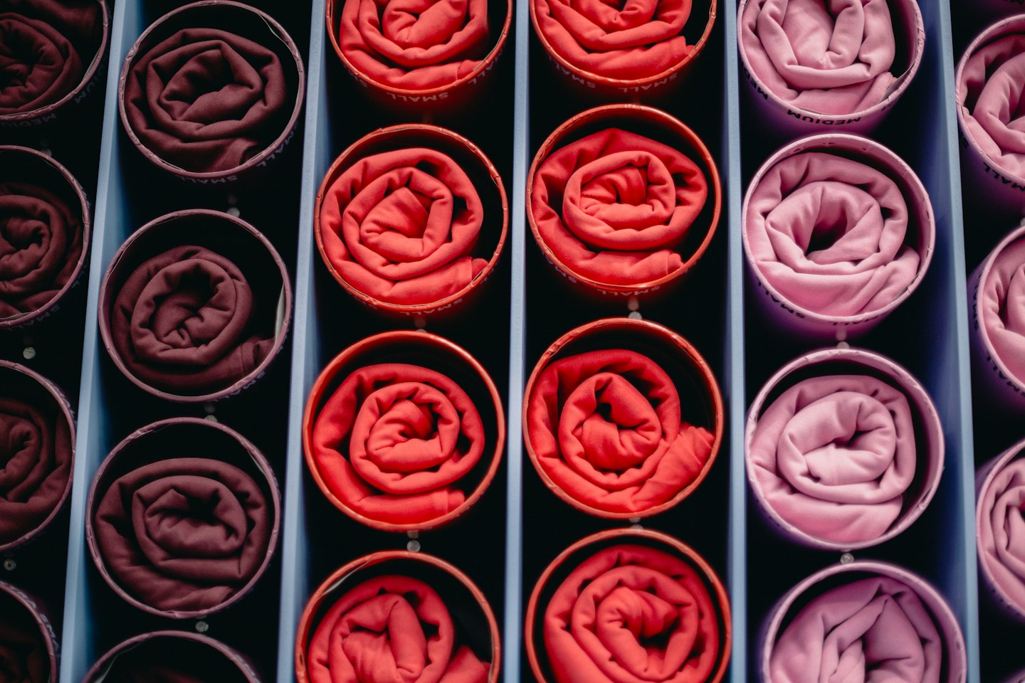 Magliette arrotolate e organizzate per colore in uno scaffale.